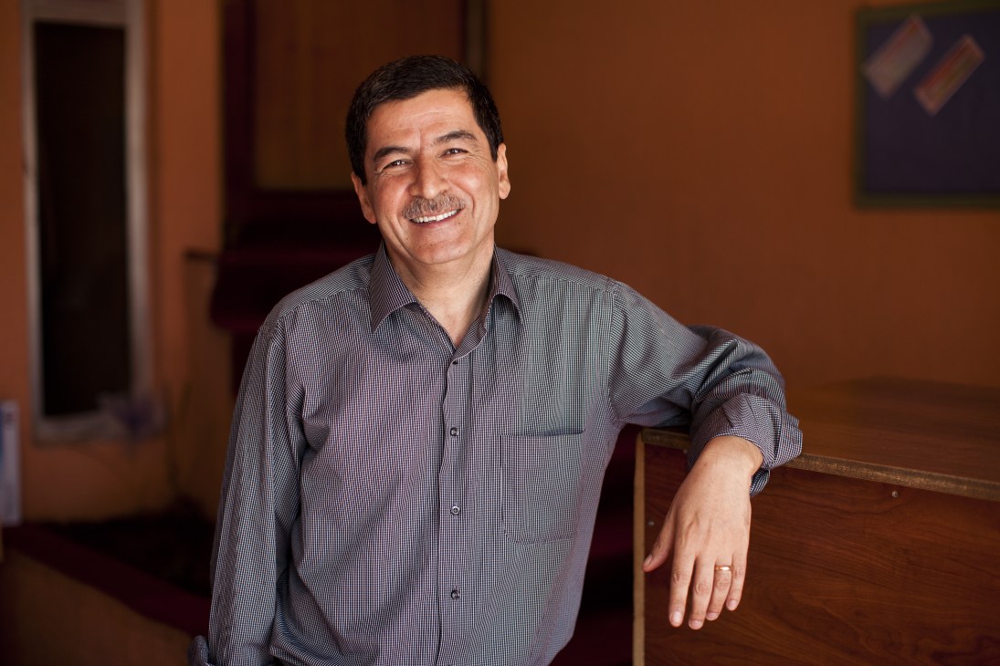 Asos Hardi, founder of Awene newspaper, smiles while leaning against a wooden railing in an interior space.