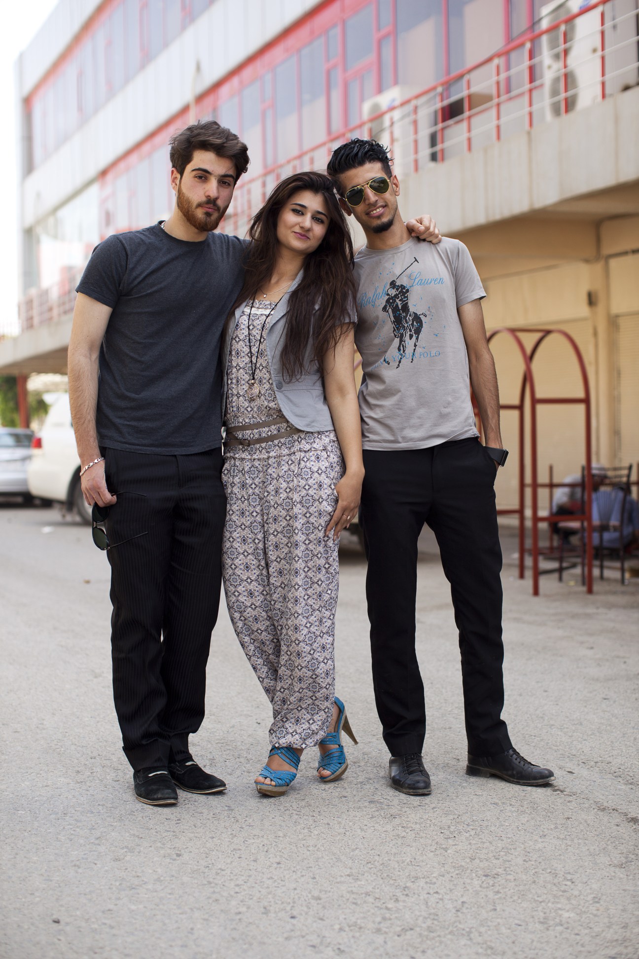 Three young people standing together on a street in front of a modern building, smiling at the camera.