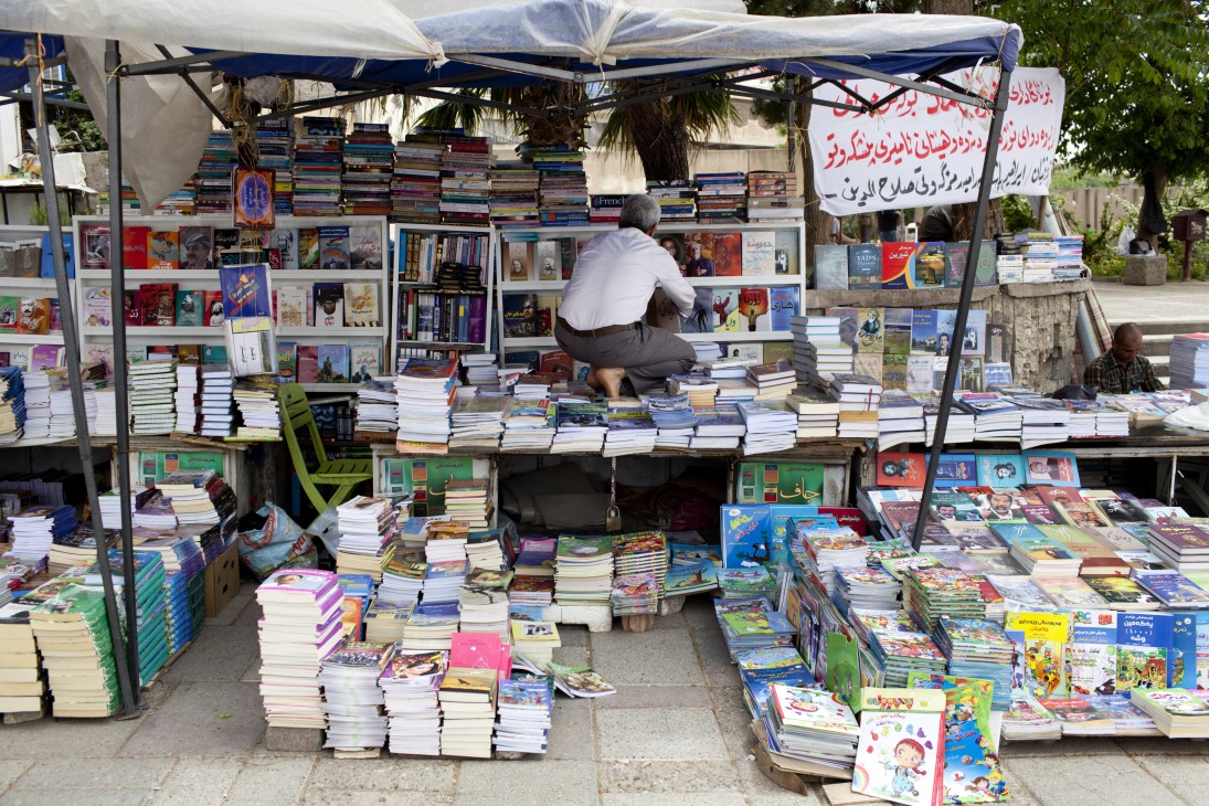 Bookseller arranging books and magazines at an outdoor market stall in Sulaymaniyah bazaar