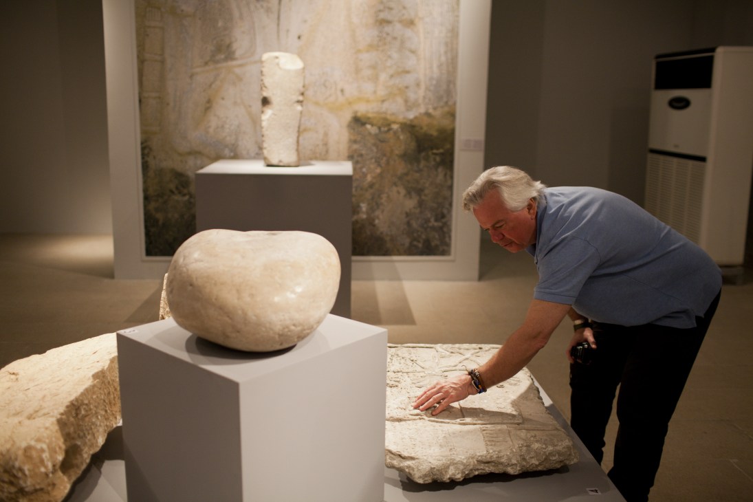 An older man examines an ancient stone artifact on display in a museum gallery.