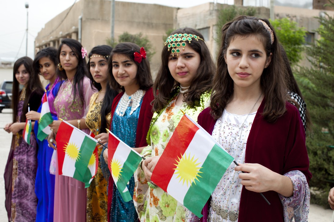Kurdish students in colorful traditional dress holding Kurdish flags at an environmental festival.