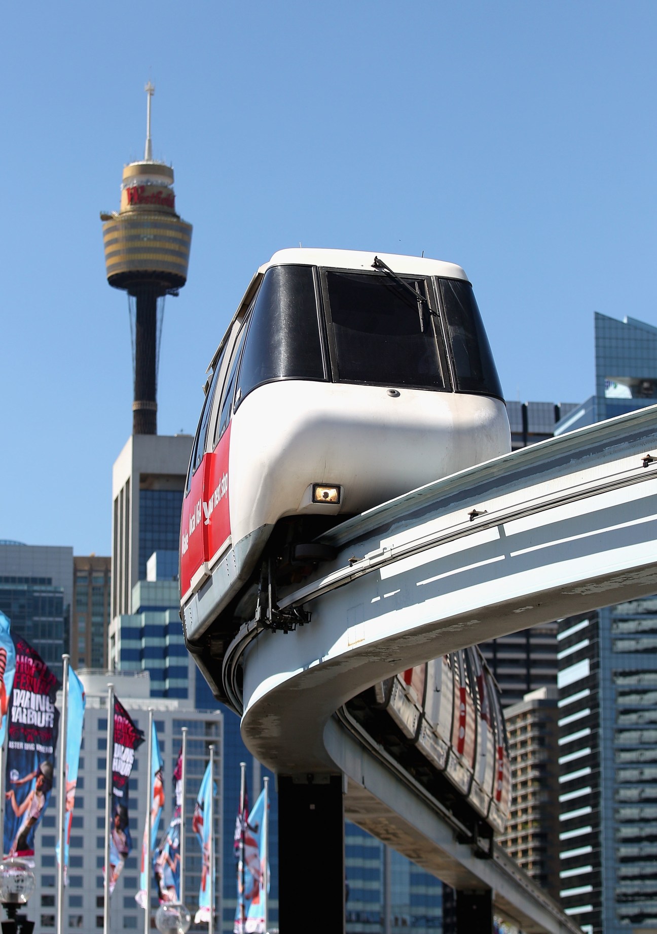 Sydney's monorail train car suspended on elevated track with Sydney Tower in background.