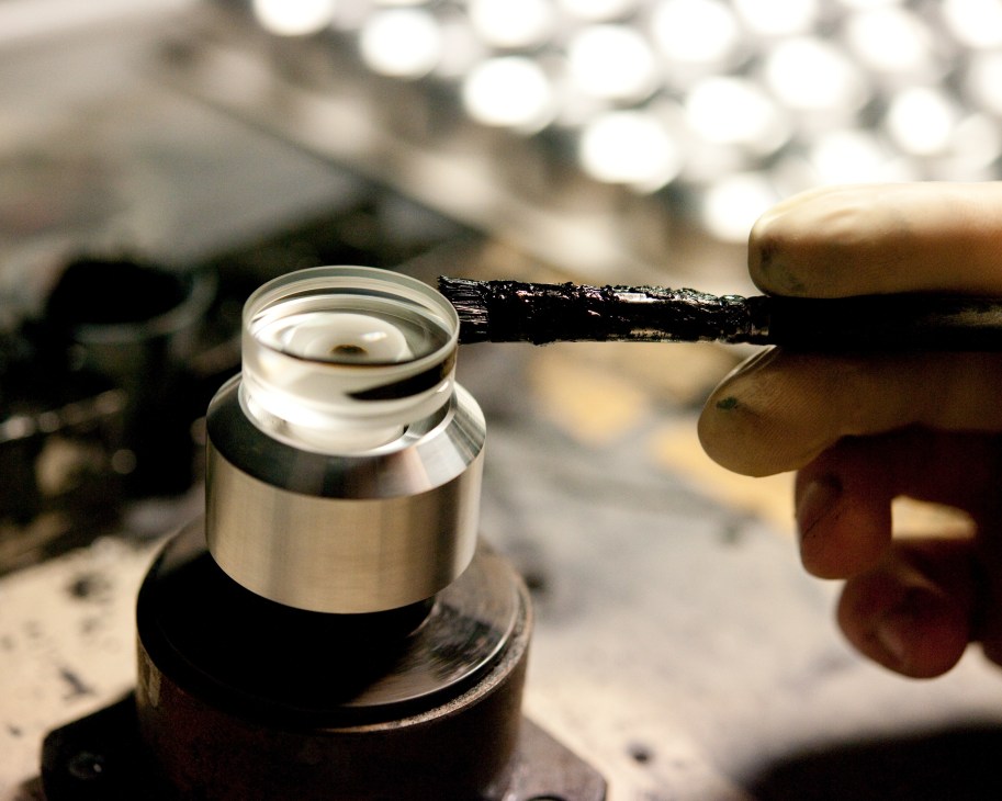 A worker paints the rim of a lens component with a brush during binocular manufacturing.