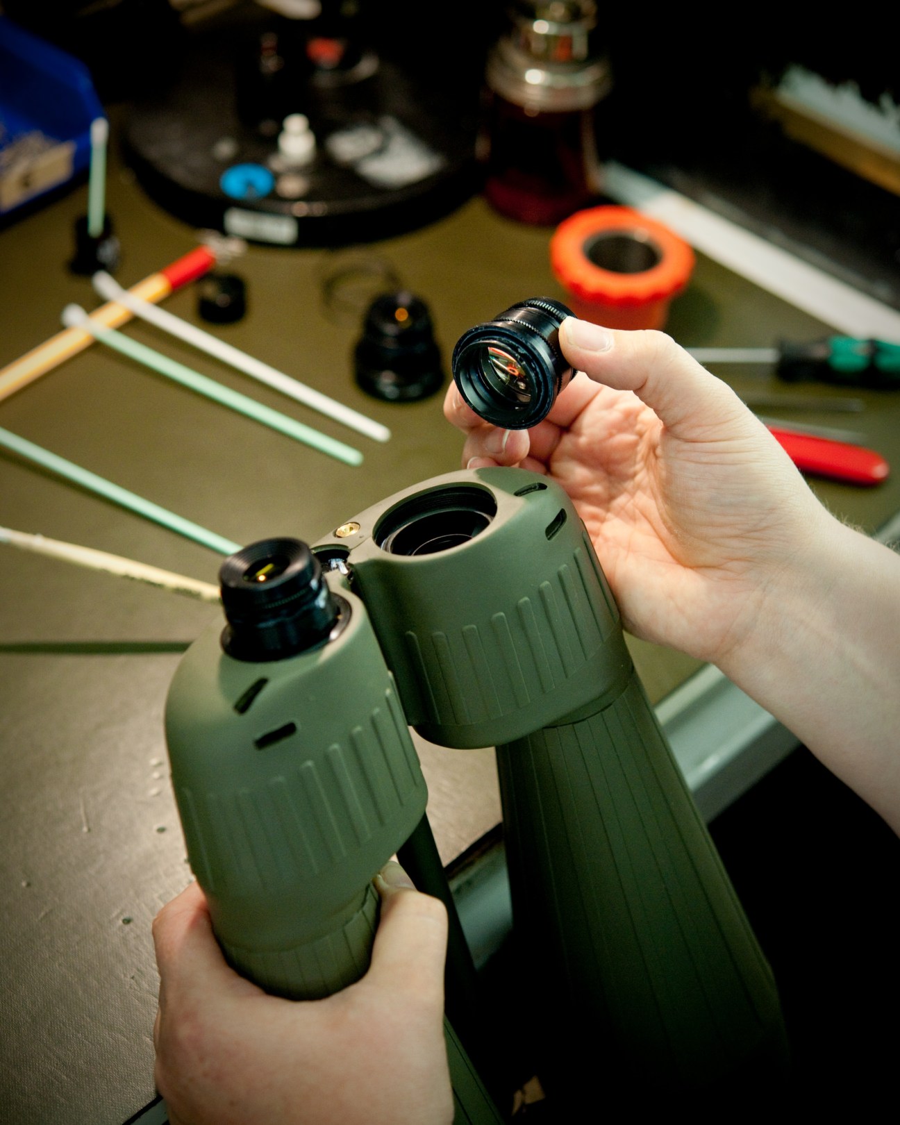 A worker's hands fit a lens assembly into a green Steiner binocular during manufacturing.