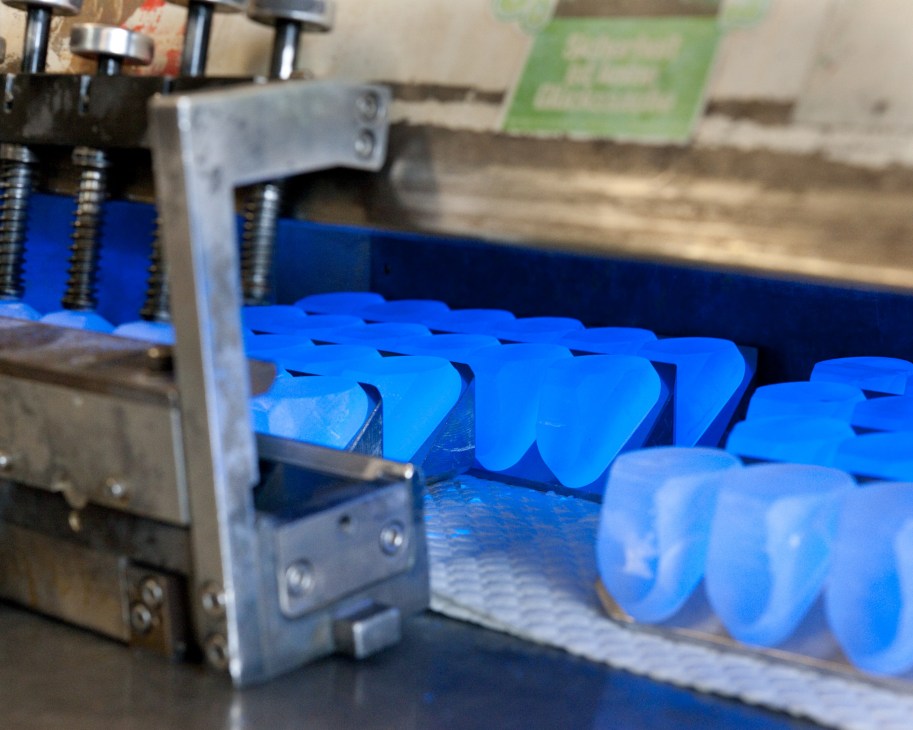 Blue glass prisms arranged in a manufacturing tray under UV light at Steiner factory.