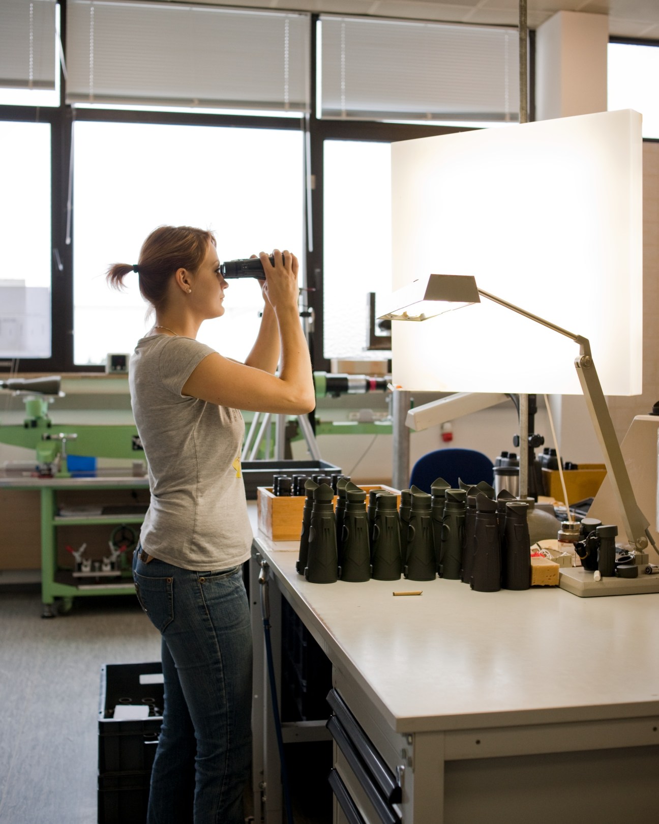Woman inspecting binoculars for defects at Steiner factory workstation.