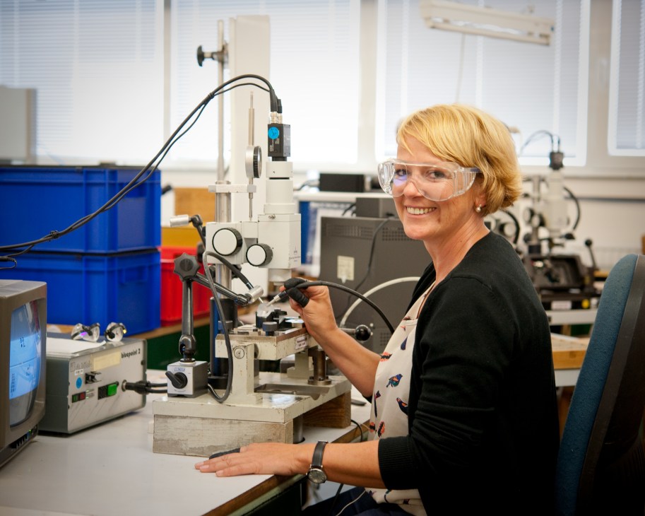 Woman in safety glasses aligns prism focal points on precision optical equipment at Steiner factory.