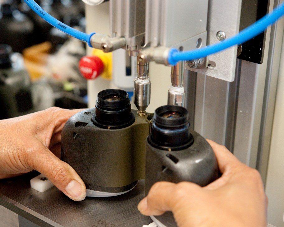 Worker blowing dried nitrogen into Steiner binoculars during assembly at the German manufacturing facility.