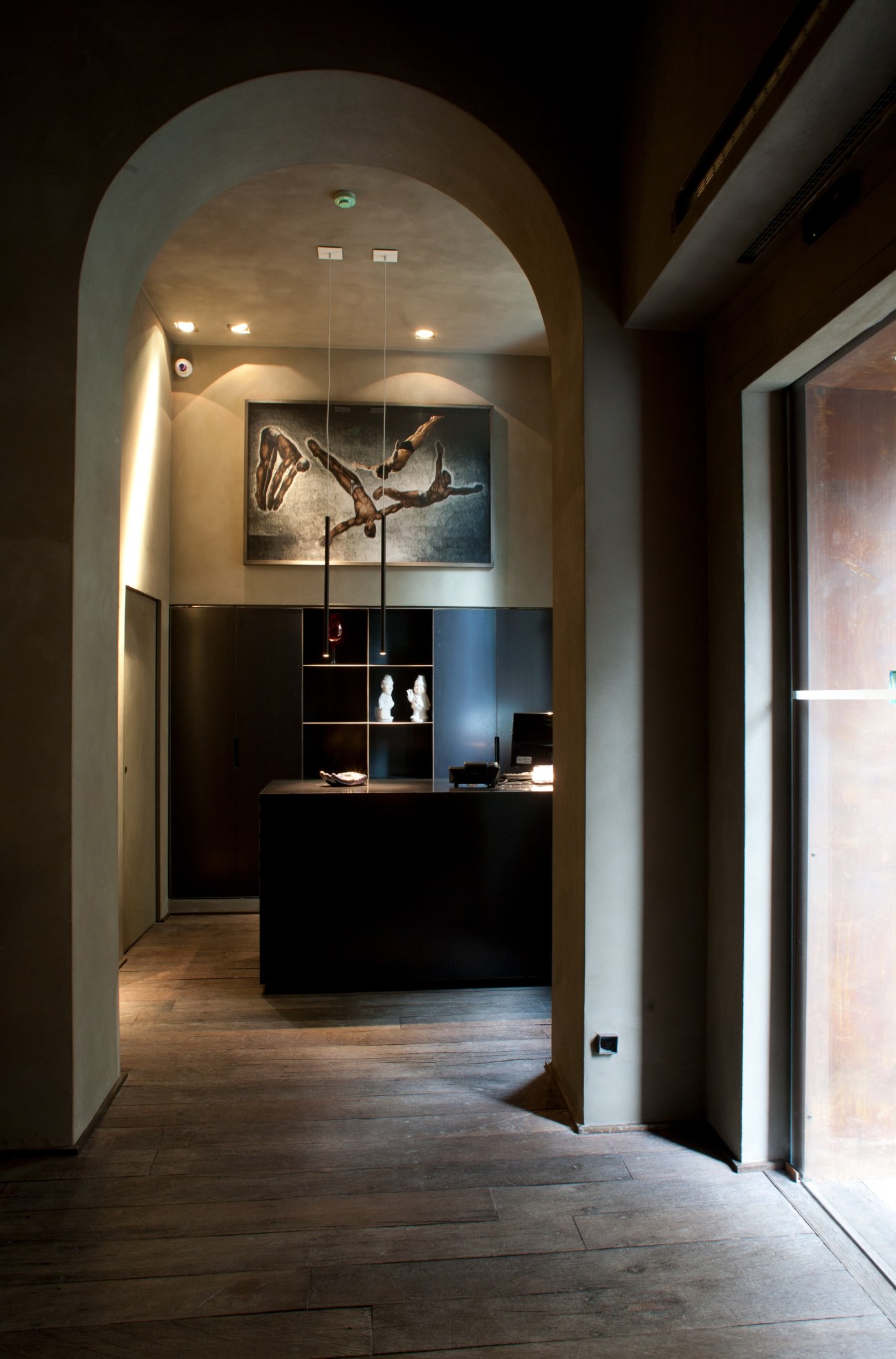 Interior of Palazzo Segreti Milan showing a modern hallway with arched ceiling, wooden floors, black modular shelving, and contemporary artwork.