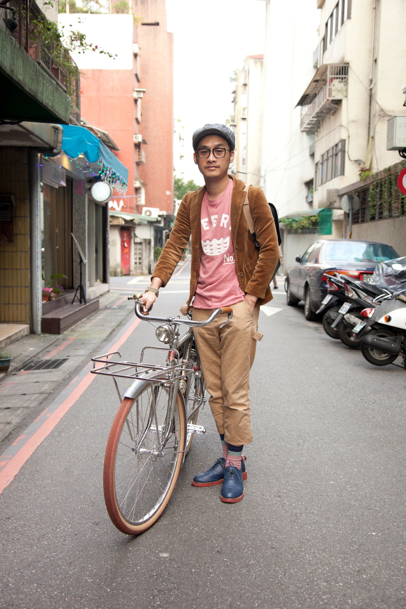 Man in brown cardigan and cap riding vintage bicycle on urban street in Taipei.