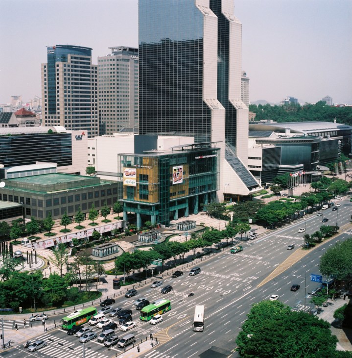 Aerial view of Seoul's COEX building and surrounding modern high-rise architecture with busy streets and green areas.