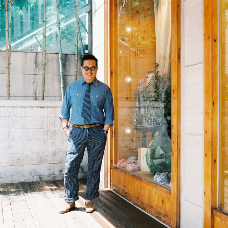 Han Taemin, director of San Francisco Market retail store, stands outside a wooden storefront with glass windows displaying merchandise.