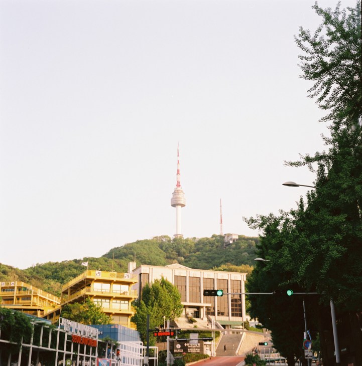 N Seoul Tower rises above Mount Namsan with surrounding buildings and green hillside vegetation.