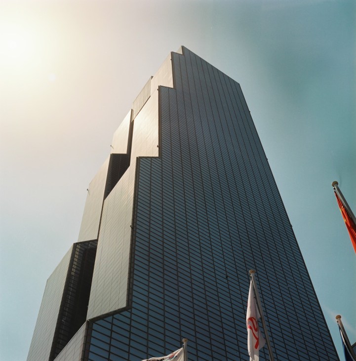 Modern skyscraper with distinctive angled white and dark grey facade against blue sky with flags.