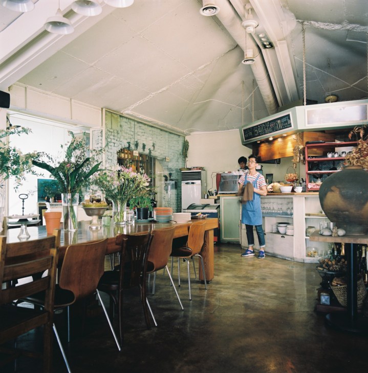 Cork for Turtle restaurant interior with wooden dining table, staff member, and plants.