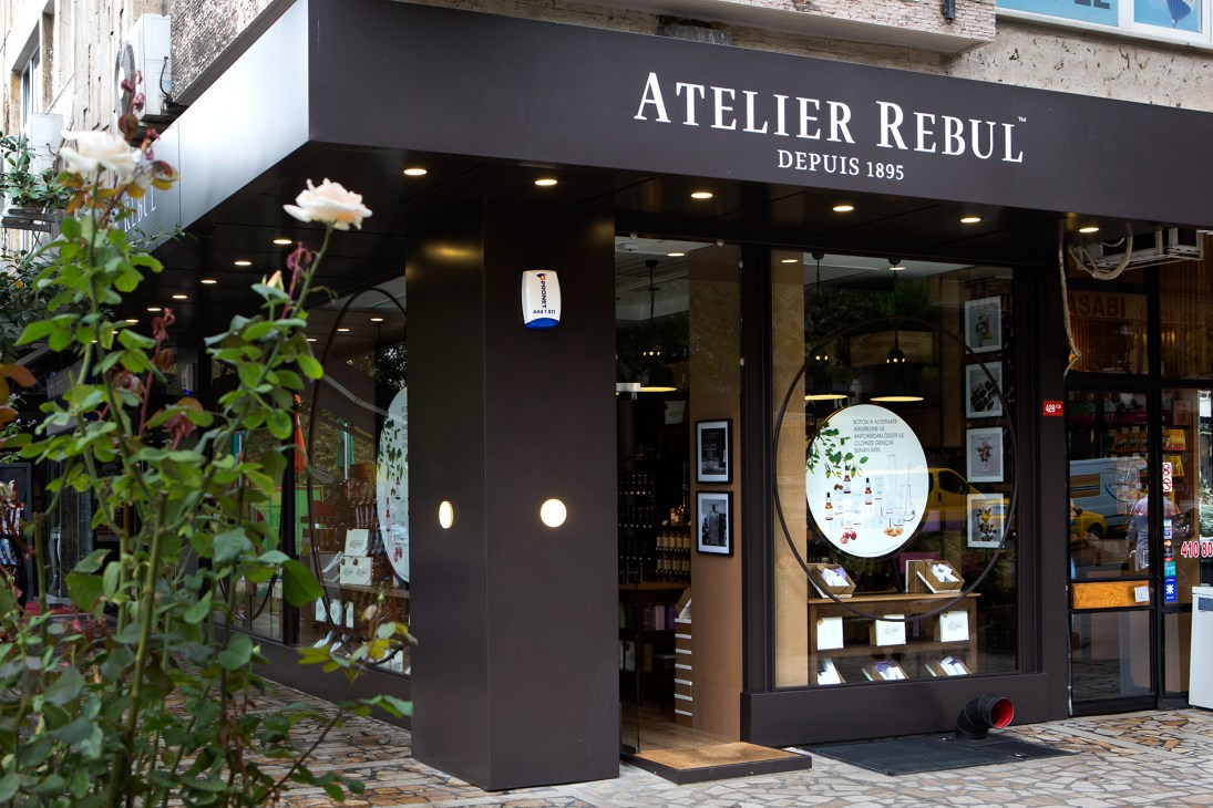 Atelier Rebul storefront with black awning reading 'ATELIER REBUL DEPUIS 1895' and illuminated window displays.