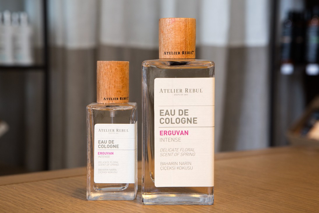 Two Atelier Rebul Erguvan Intense eau de cologne bottles with wooden caps displayed on a wooden surface.