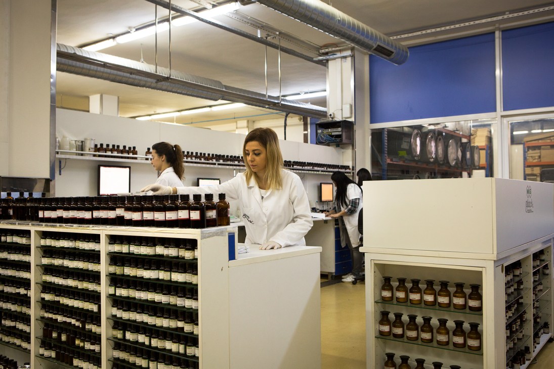 Laboratory technician in white coat working at the Gulcicek fragrance factory with shelves of ingredient bottles.