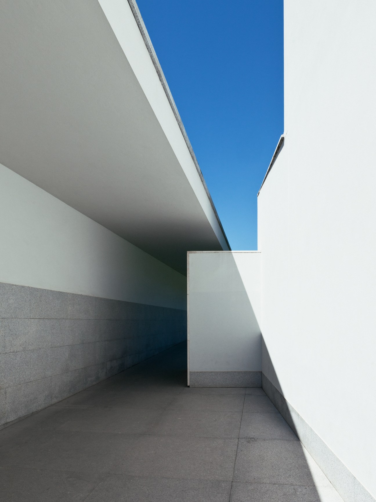 Minimalist white concrete entrance to Serralves Foundation museum with curved walls and clear blue sky.
