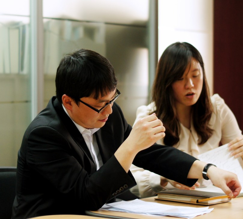 Two ministry officials review documents at a desk in an office setting.