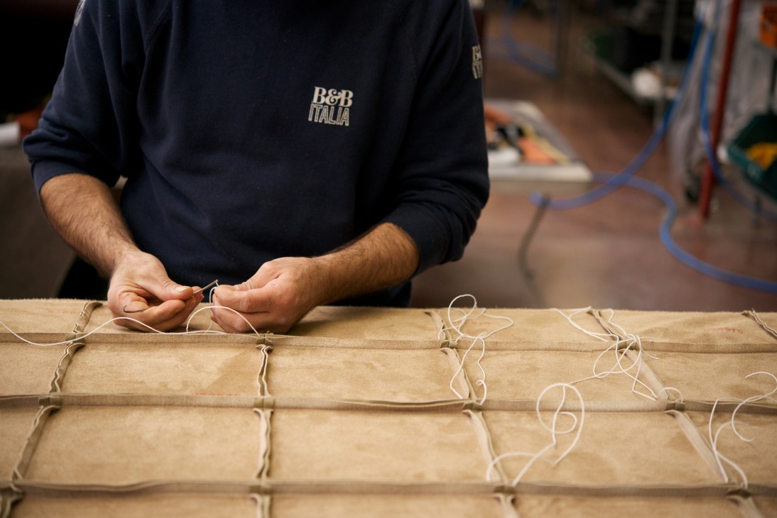 B&B Italia worker hand-sewing leather upholstery with needle and thread on a cushion panel.