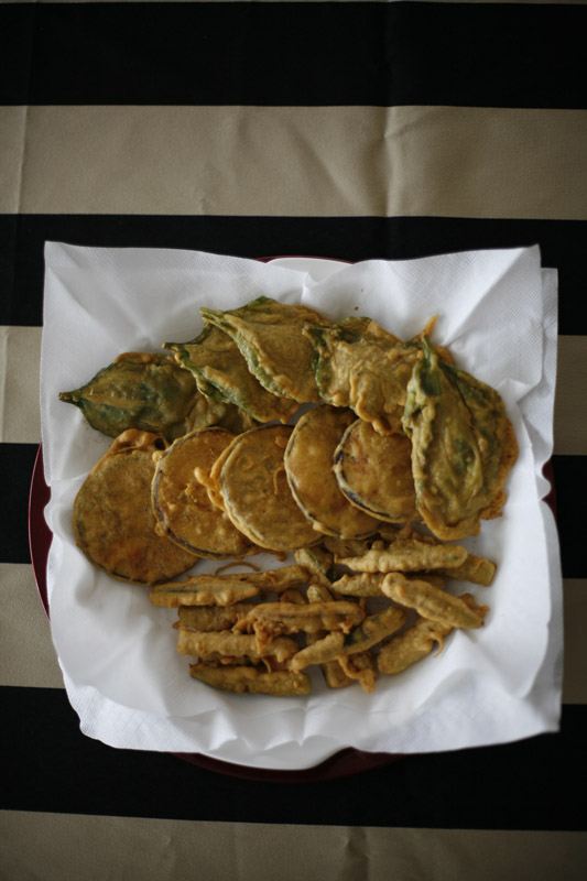 Deep-fried pakoras of spinach, aubergine and okra served on white paper.