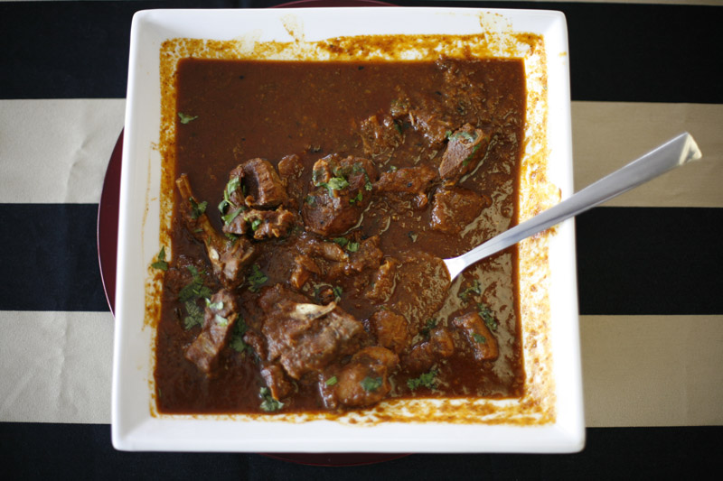 Bowl of Subodh Gupta's lamb curry garnished with green coriander on a striped background.