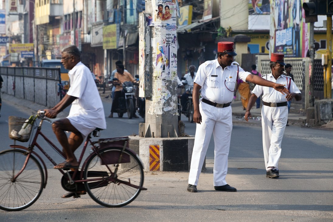 Pondicherry policeman in white French-style uniform with red kepi directs traffic on an Indian street.