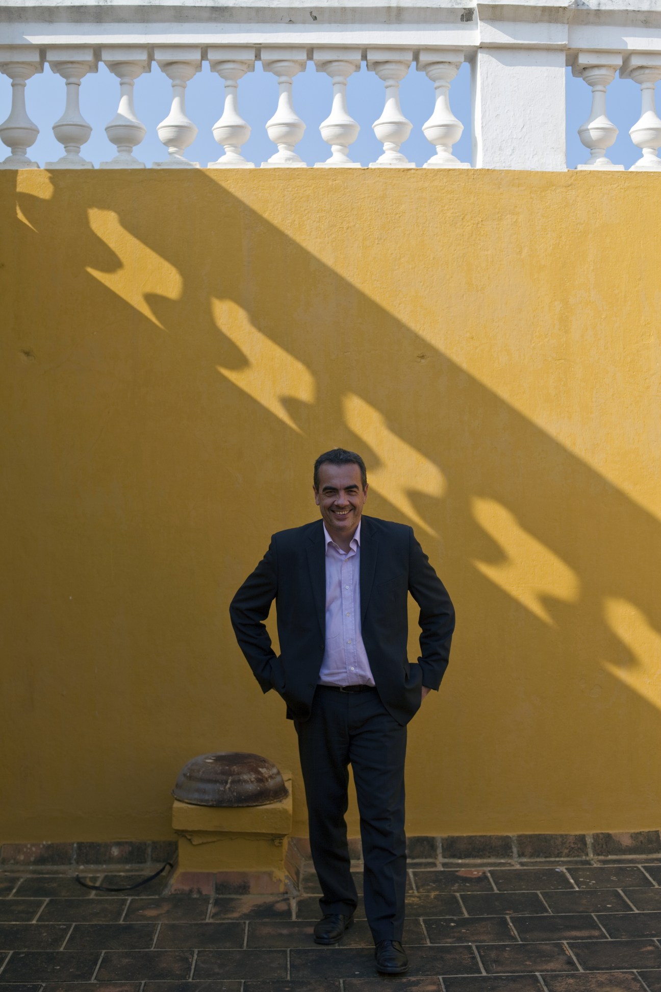 Pierre Fournier, French consul general, stands in front of a yellow colonial wall with white balustrade railing at the French Consulate in Pondicherry.
