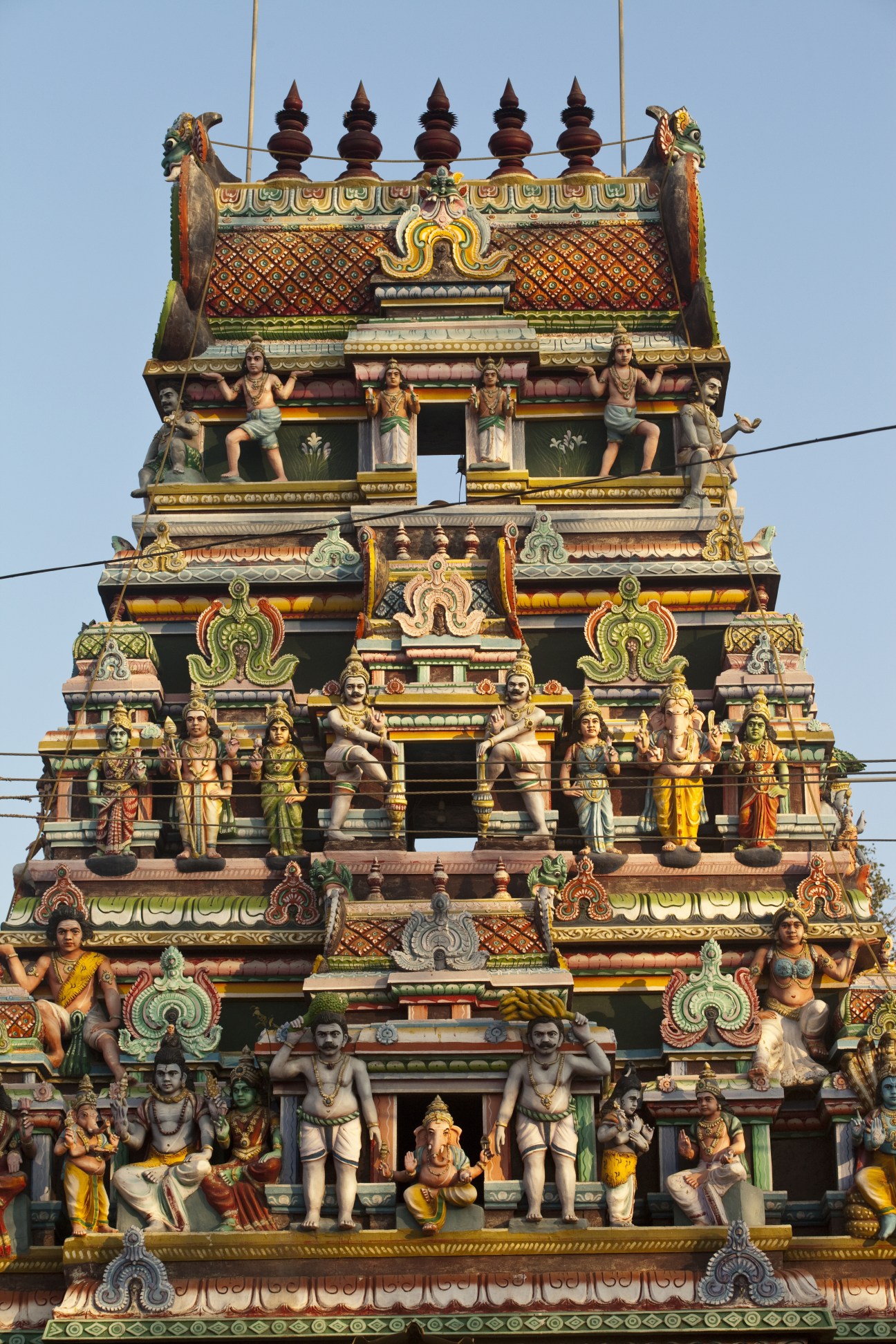 Ornate South Indian temple gopuram with colorful sculptural deities, golden finials, and intricate architectural details.