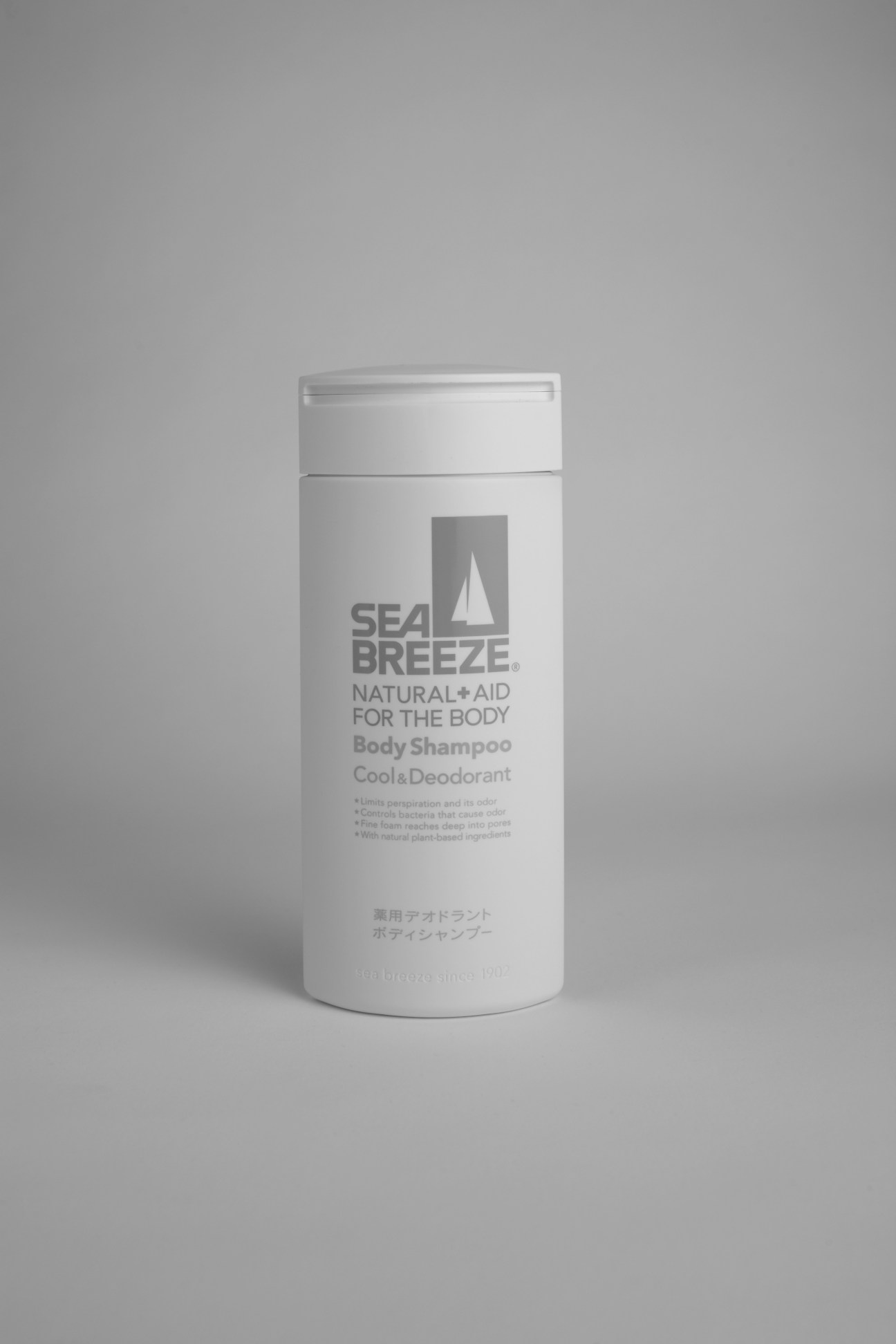 White cylindrical bottle of Sea Breeze Body Shampoo with sailboat logo and product text on gray background.