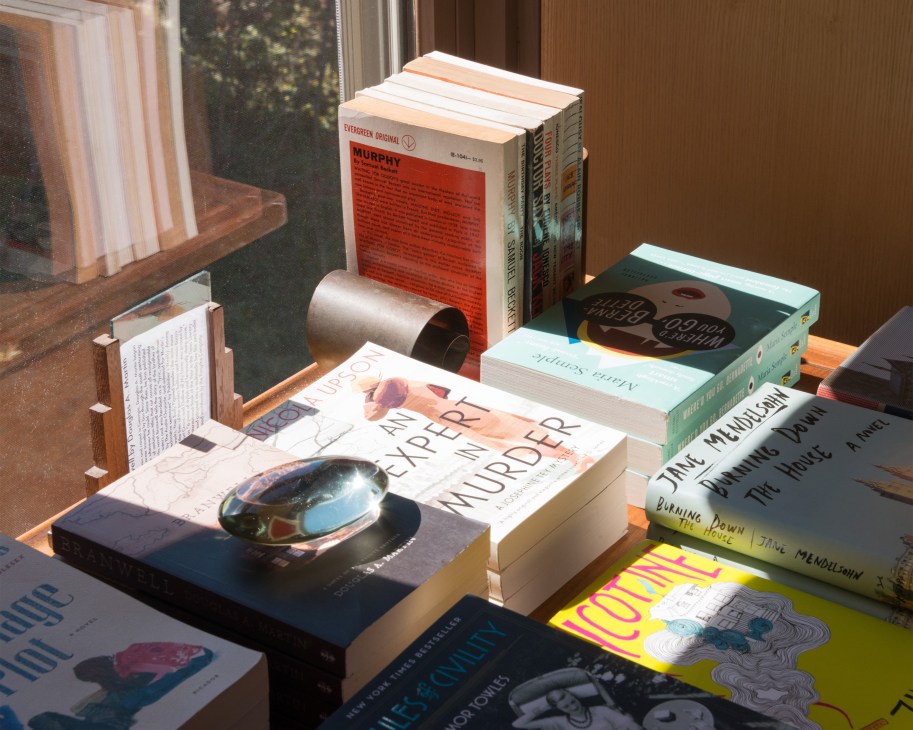 Curated books displayed on a wooden shelf with natural light from a window at One Grand bookstore.