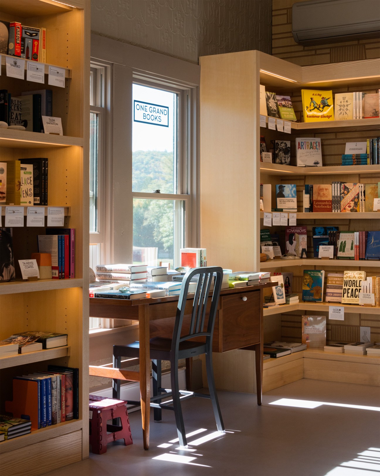 One Grand bookshop interior with wooden shelves, desk, and window displaying the store's logo.