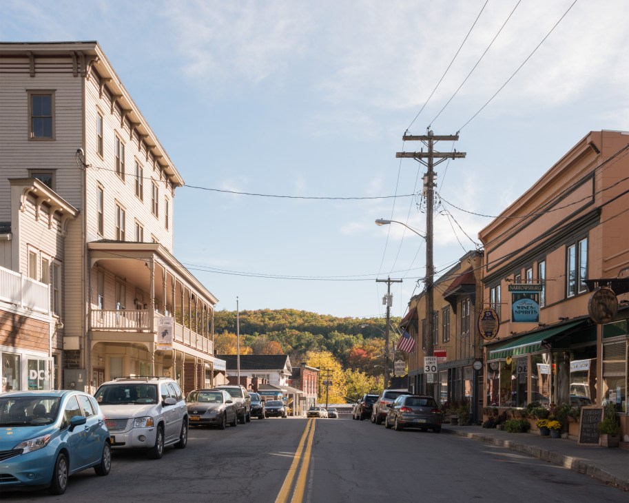 Main Street in Narrowsburg lined with historic brick and wooden buildings, parked cars, and forested hills in the background.