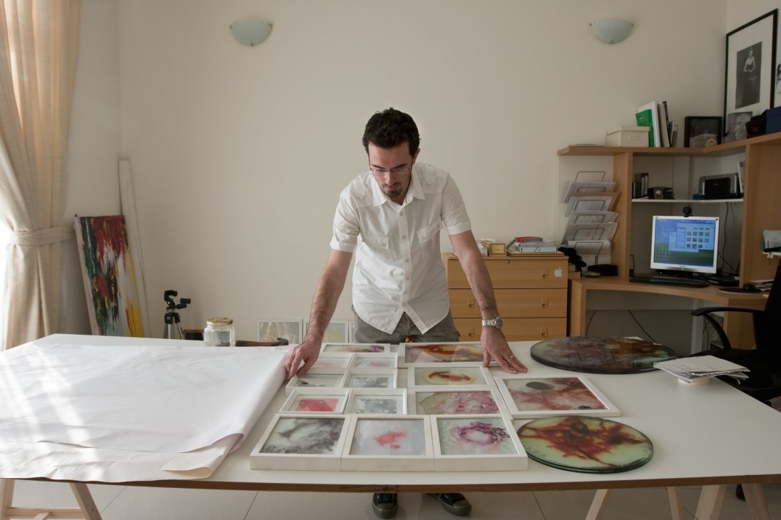 Man in white shirt examining framed artwork samples on a studio table.