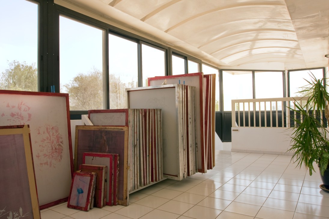 Sunlit art studio space with framed silkscreens and canvases leaning against walls beneath curved skylights at Tashkeel.