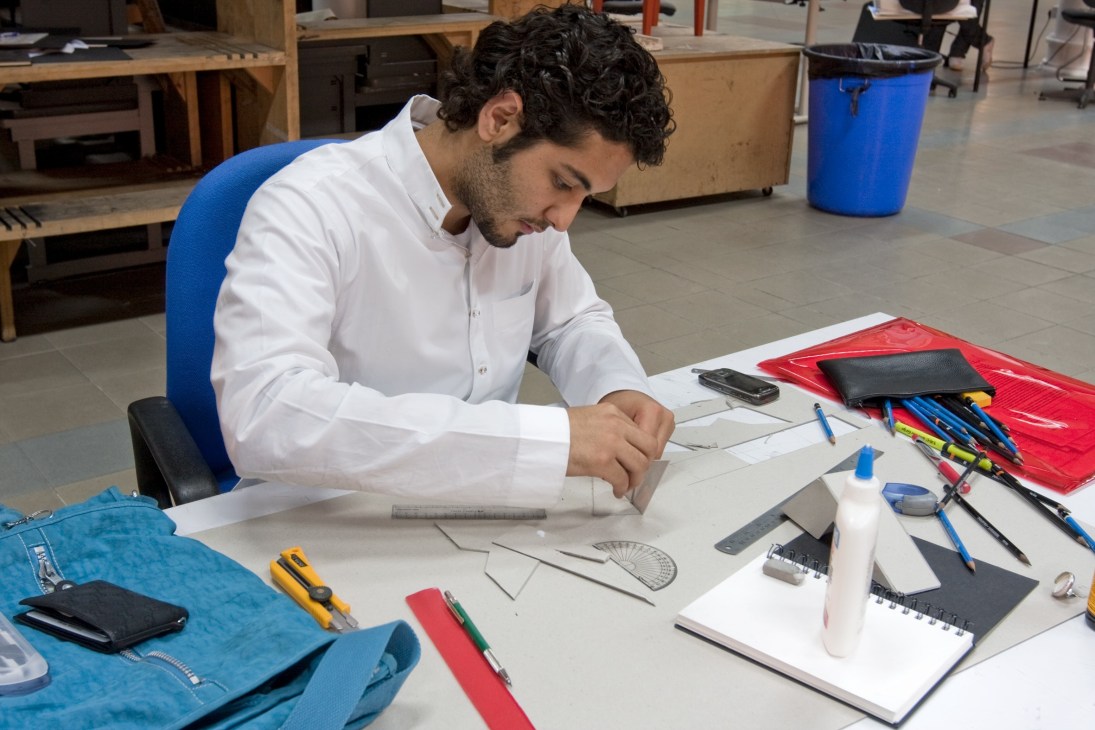 Design student Mansour Bakheet works at a table with sketches, rulers, and art supplies.