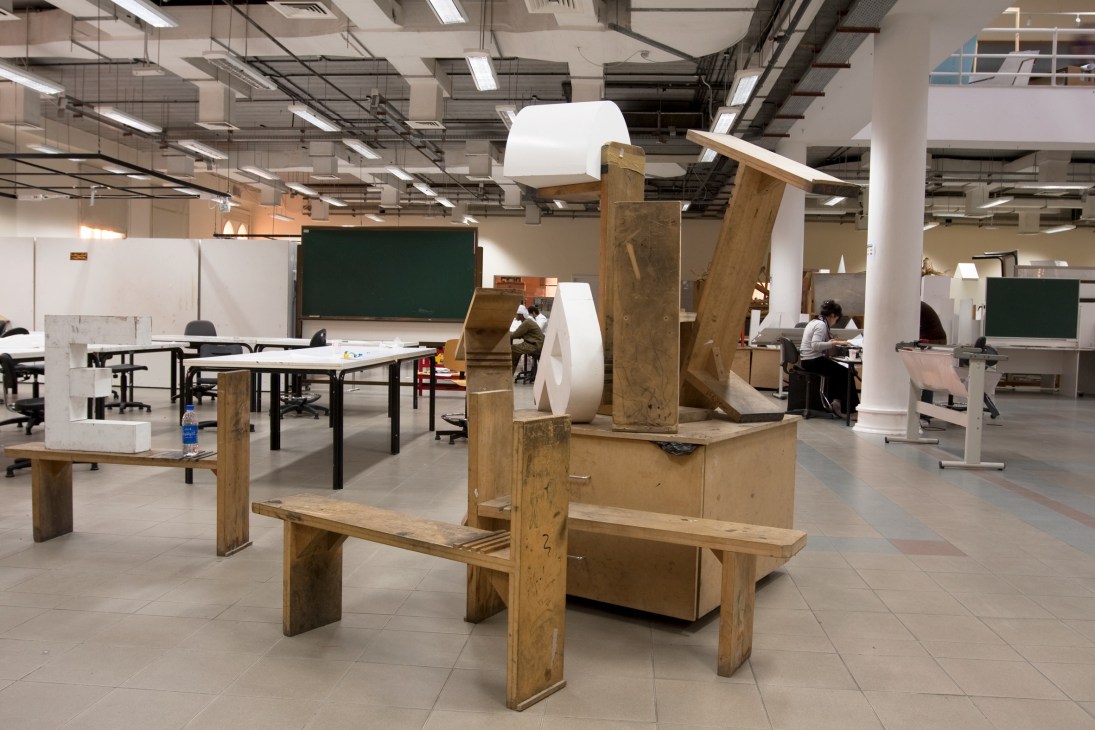 A studio space with wooden sculptural installations, work tables, and students studying amid art installations and green chalkboards.