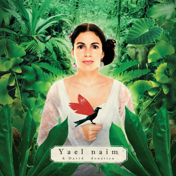 Album cover for Yael Naim's "She Was a Boy" featuring a woman in white surrounded by lush green jungle foliage and a red-winged bird.