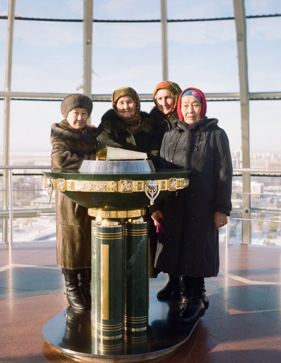 Four women in winter coats and headscarves place their hands on a gold-plated handprint plinth at the Bayterek Tower observation deck in Astana.