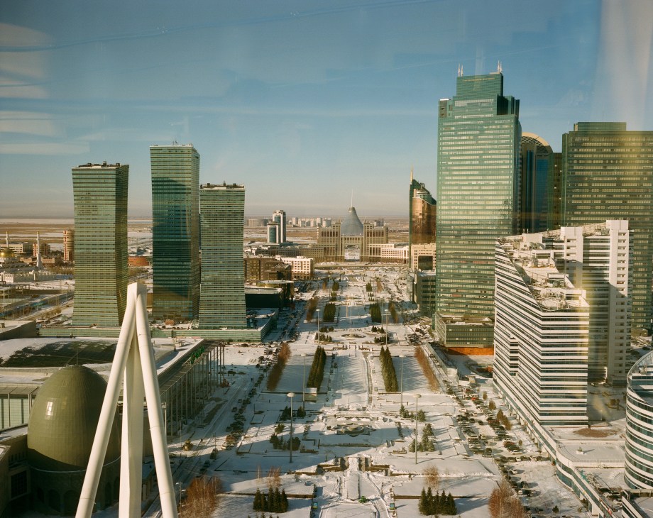 Aerial view of Nurzhol Boulevard in Astana showing modern glass towers, wide boulevards, and sparse landscaping in a vast flat desert landscape.