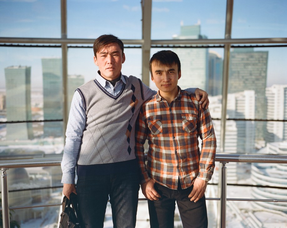 Two men stand by a high-rise window overlooking Astana's skyline of modern buildings.