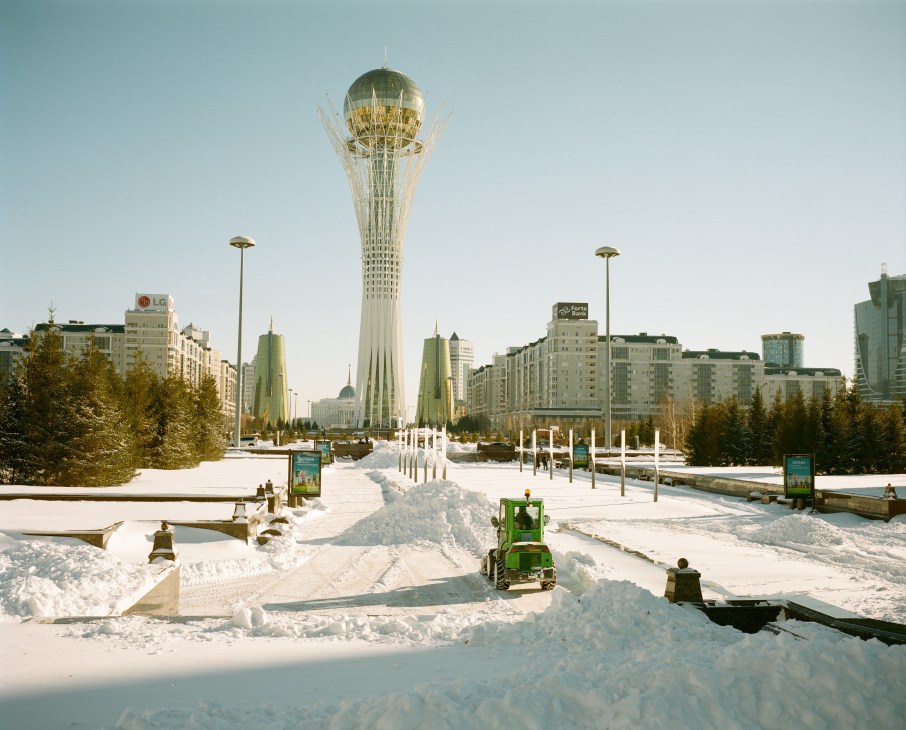 Snow-covered Nurzhol Boulevard in Astana with the Bayterek Tower rising centrally, flanked by modern buildings and cleared pathways.