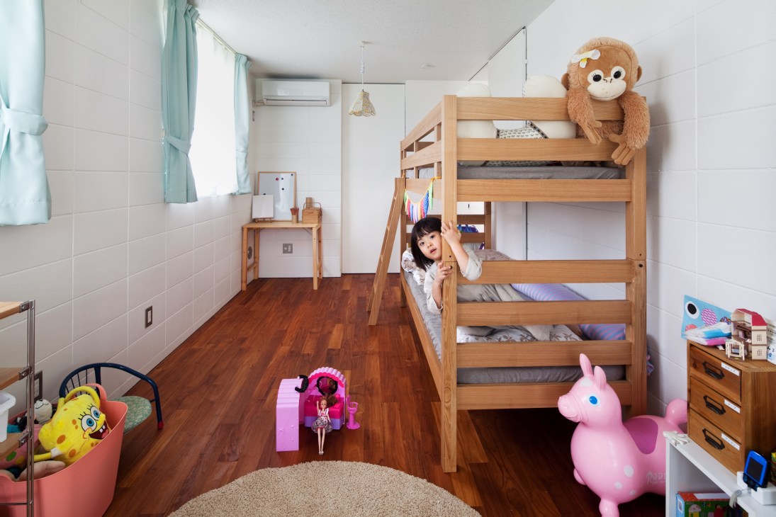 Child playing in a bright bedroom with white tiled walls, wooden bunk bed, and teak flooring in an Okinawa Standard house.