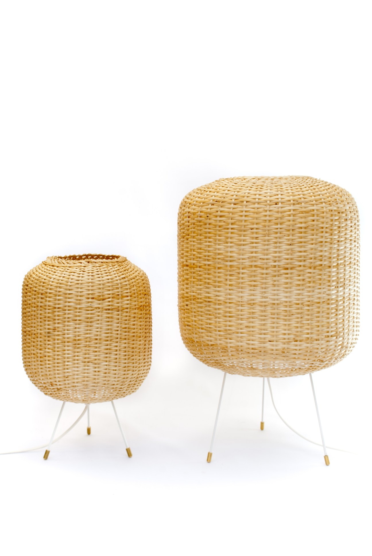 Two handmade woven wicker lights in natural tan color with white metal tripod legs and brass accents.