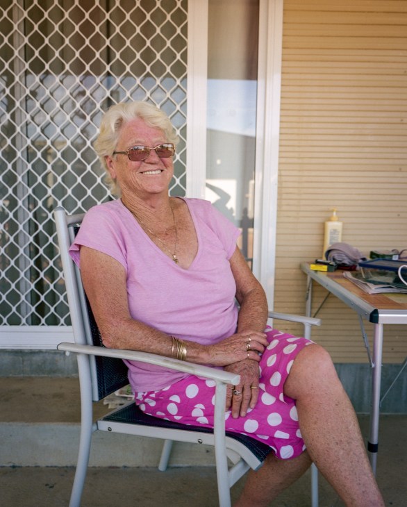 Shirley Embrey, a 69-year-old woman with white hair and sunglasses, sits smiling in a chair on a porch.