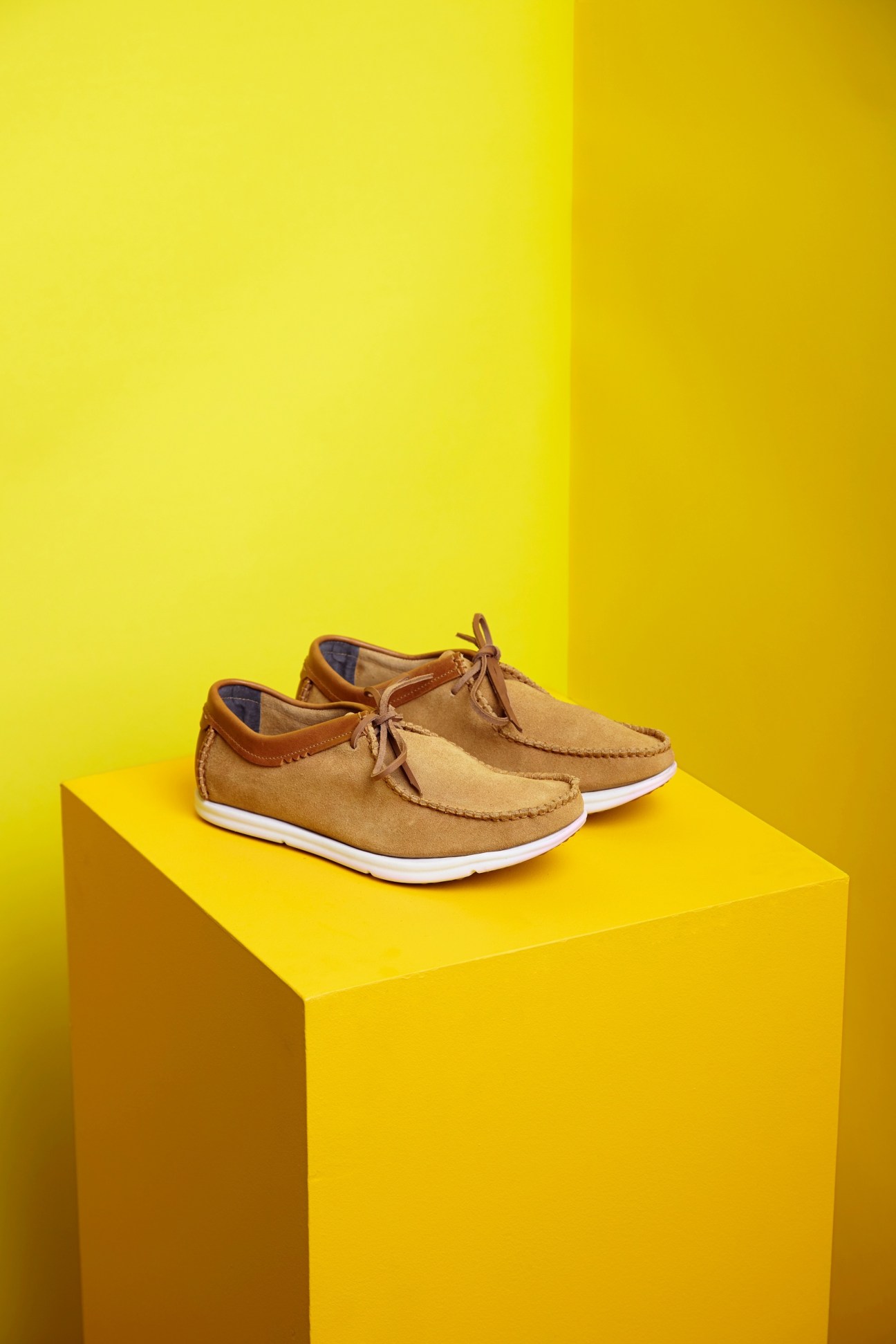 Pair of tan suede Ohw? shoes with brown leather trim and white sole on yellow block.