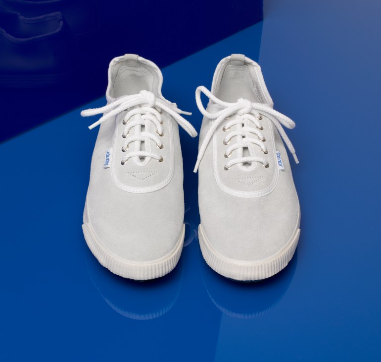 Pair of white Startas plimsolls with white laces on a blue background.