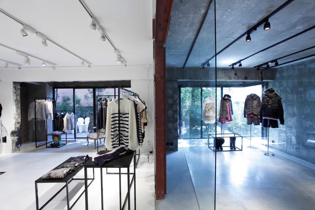 Interior of Sacai's Tokyo store showing split-level spaces with concrete and glass design, clothing displayed on racks.