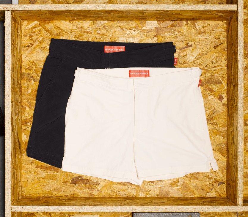 Two Orlebar Brown swimming shorts in black and white displayed in a wooden box with cork backing.